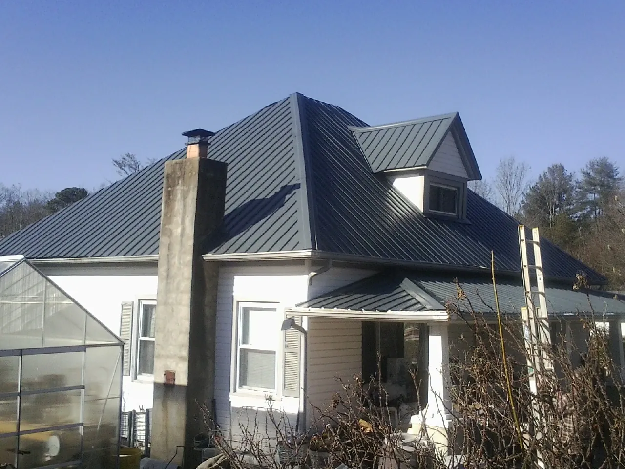 Dark blue standing seam metal roof on a white farmhouse with dormer — Slate & Tile Roof Repair by Roofing Brothers in Big Piney