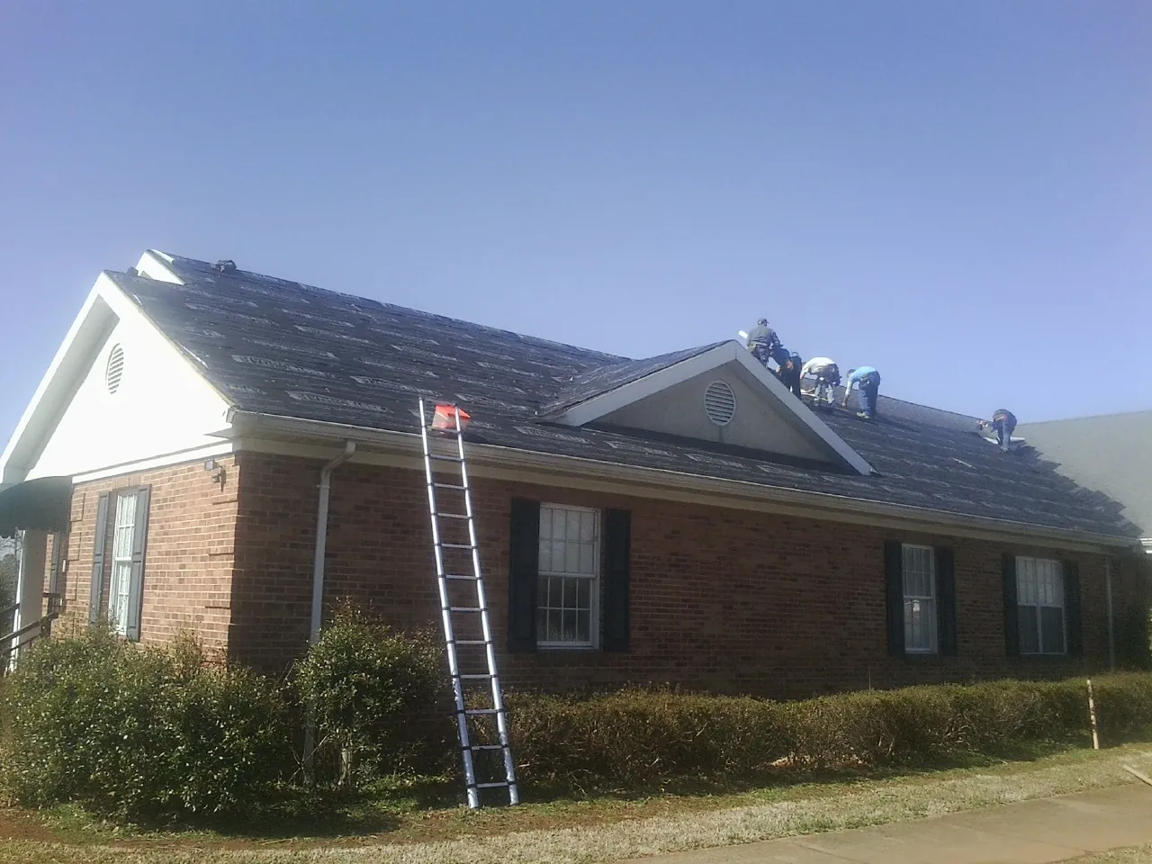 Crew tearing shingles off a brick ranch roof with a ladder set — Emergency Roof Repair work by our crew in Big Piney