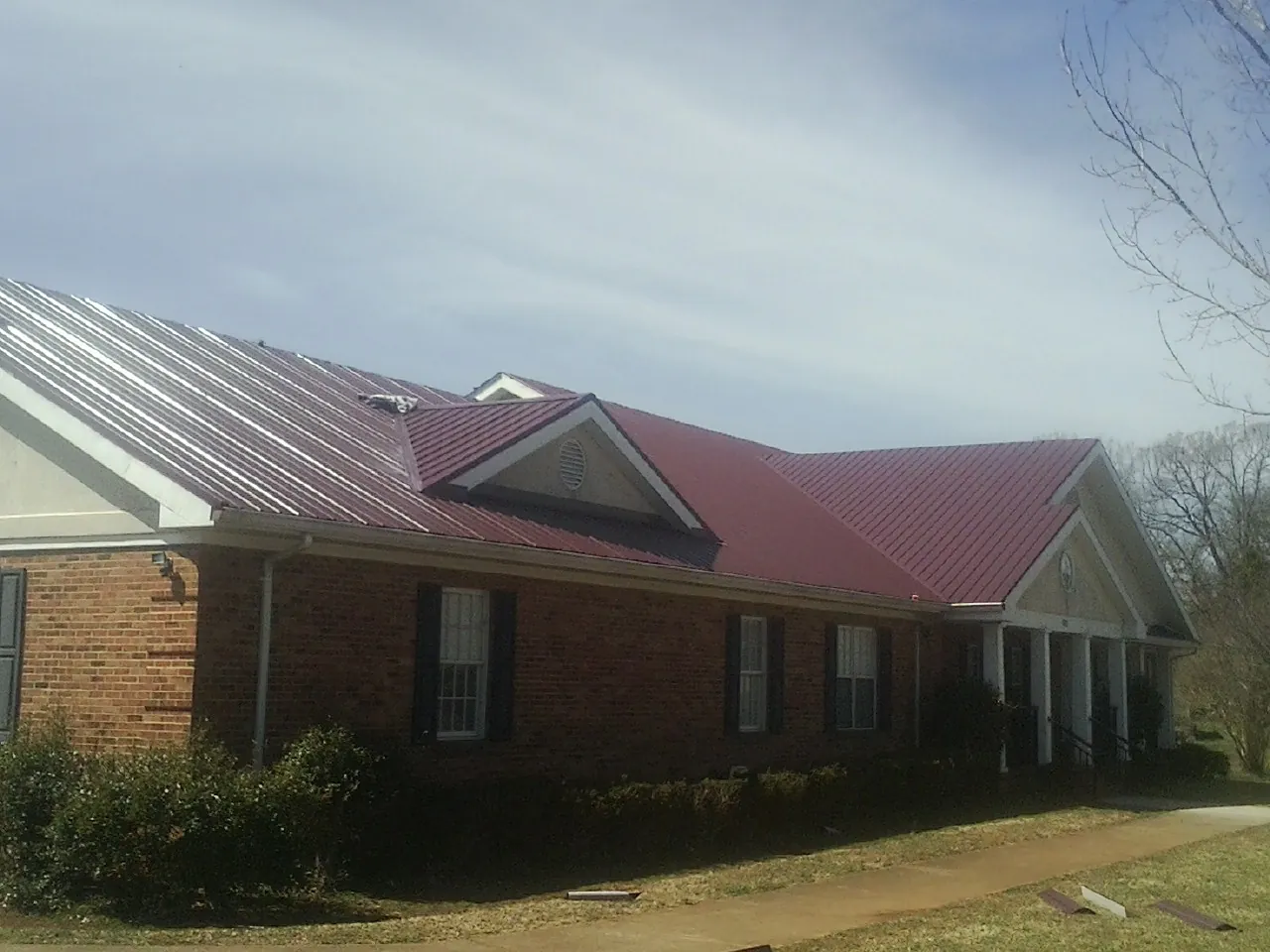 Red metal roof with gabled entries on a long brick building, from a Hail Damage Roof Repair job in Big Piney