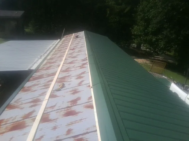 Old rusted panels beside newly installed green metal roofing — Wind Damage Roof Repair by Roofing Brothers in Big Piney