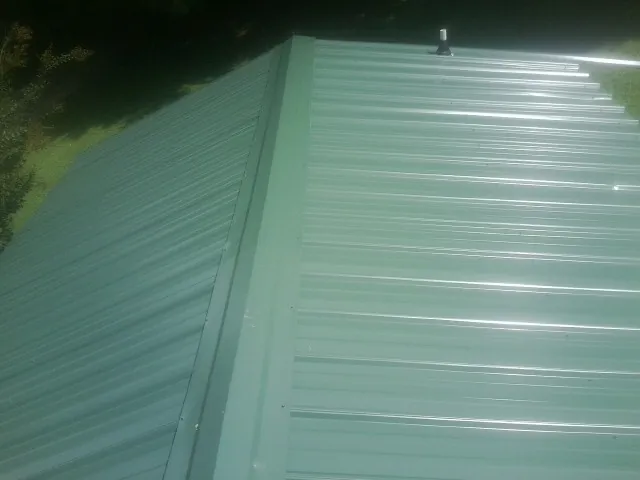 New green metal panels meeting at the ridge of a roof — Flat Roof Repair work by our crew in Big Piney