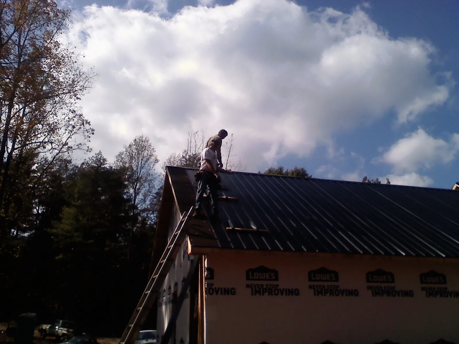 Roofer fastening dark metal panels high against a cloudy sky, from a Roof Inspection job in Big Piney