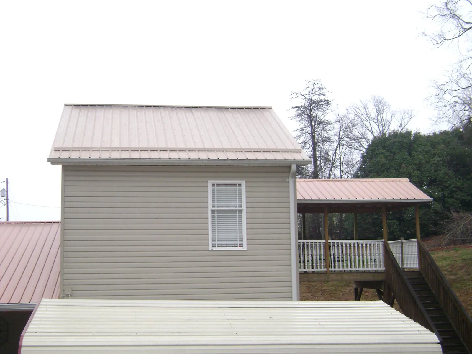 Tan metal roofs on a two story addition and attached porch, from a Roof Replacement job in Big Piney